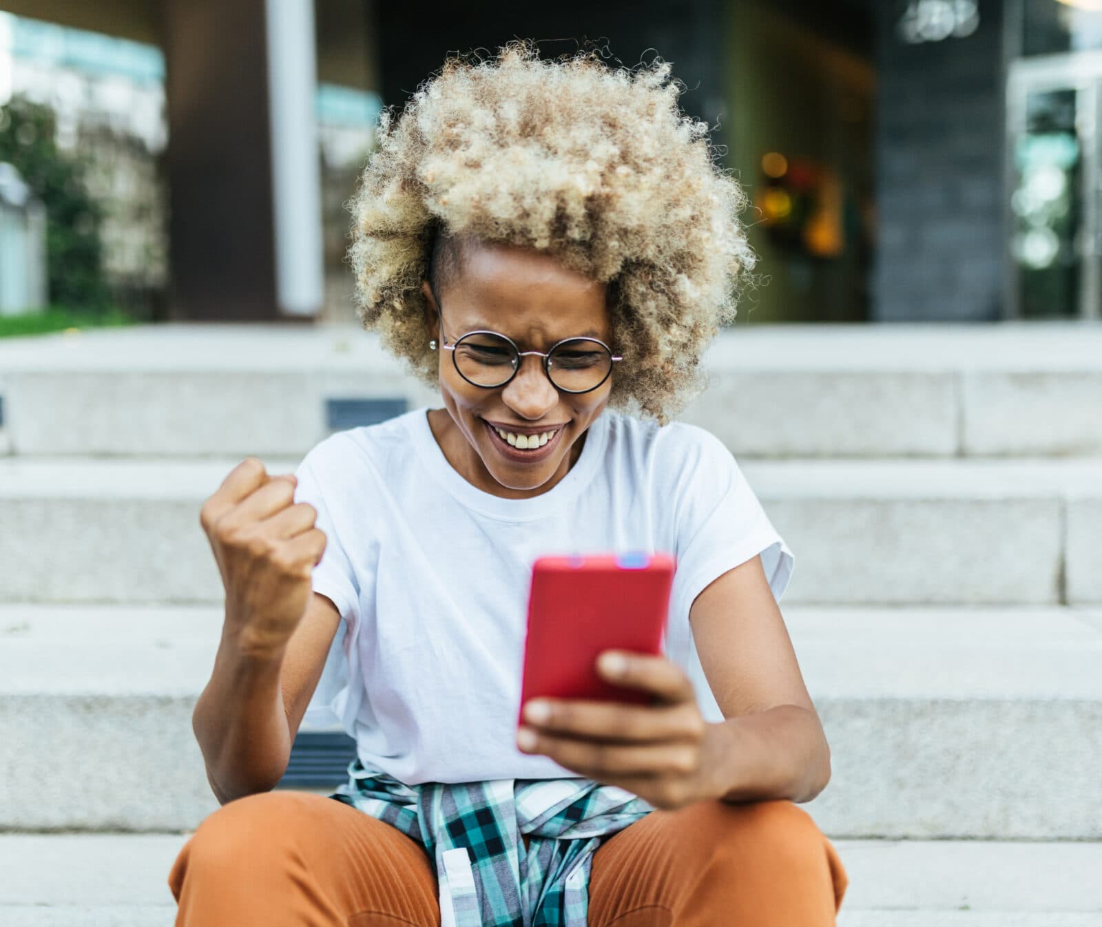 Happy afro woman celebrating victory while receiving good news on her mobile phone. Technology and success concept.