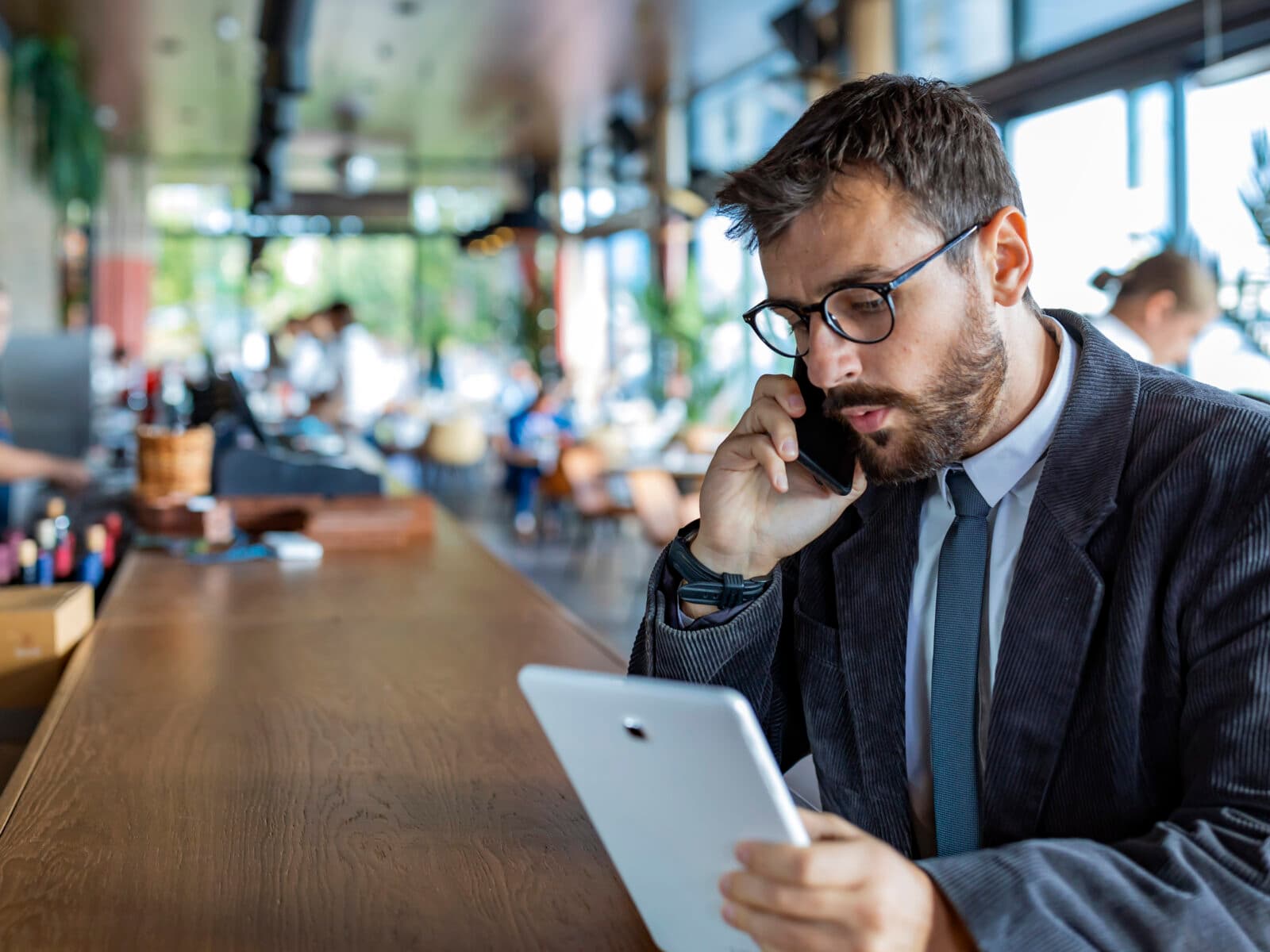 Happy and Successful Male Business Person with Beard, Dressed in Casual Suit is Communicating over a Mobile Phone and Drinking Coffee in Modern Restaurant. A Modern and Handsome Businessman is Sitting in City Café, Enjoying in Hot Cappuccino and Talking about Business with his Colleagues.